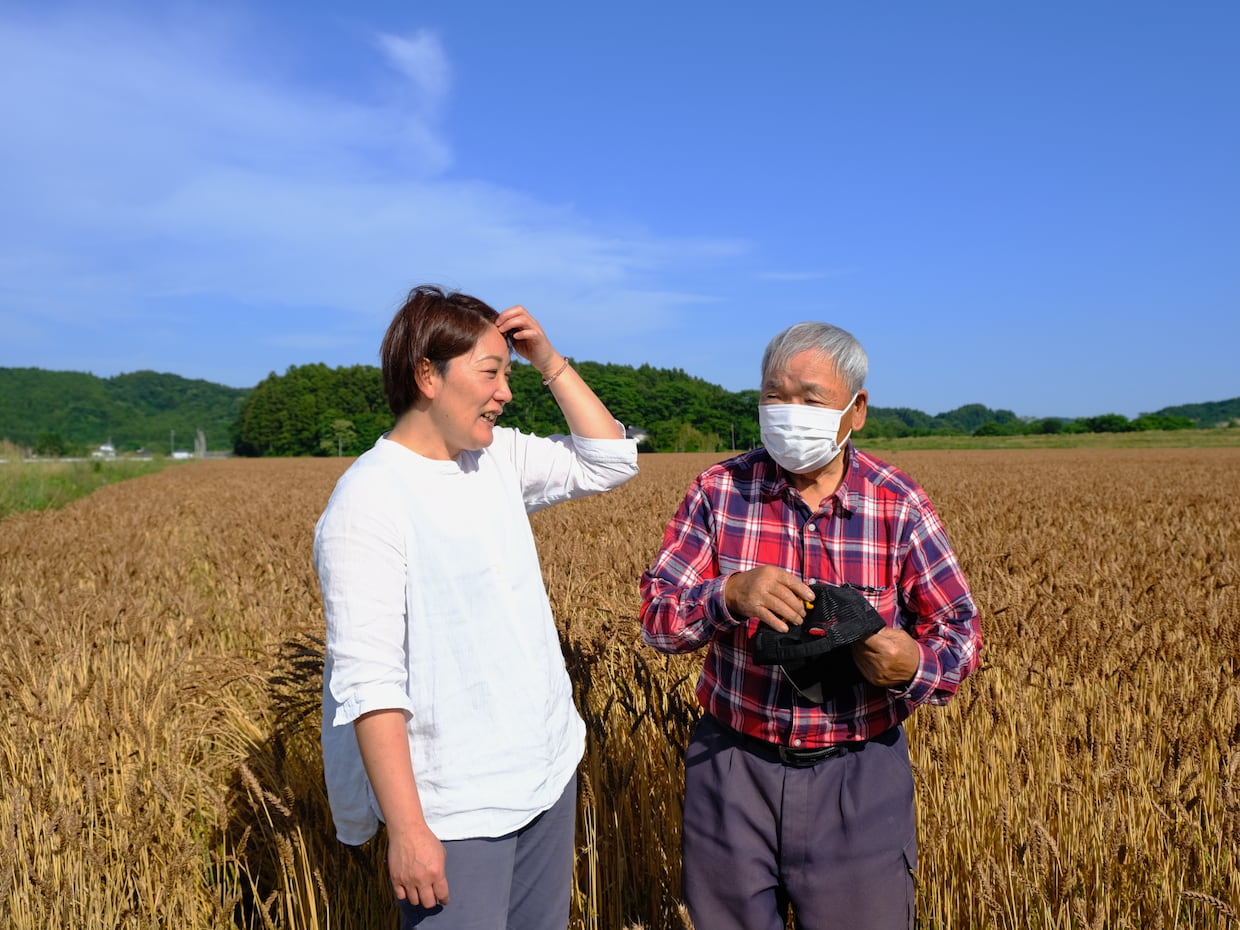 写真：麦畑の前のAuBless丹治奈緒子さんと、夏黄金の名付け親、安部瑞雄さん